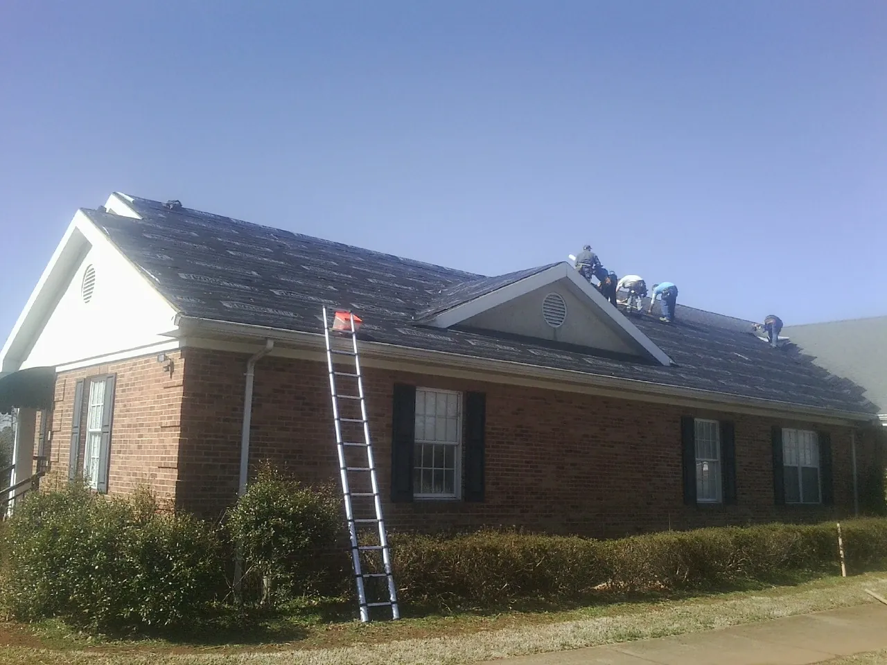 Crew tearing shingles off a brick ranch roof with a ladder set — Metal Roof Repair work by our crew in Mont Alto