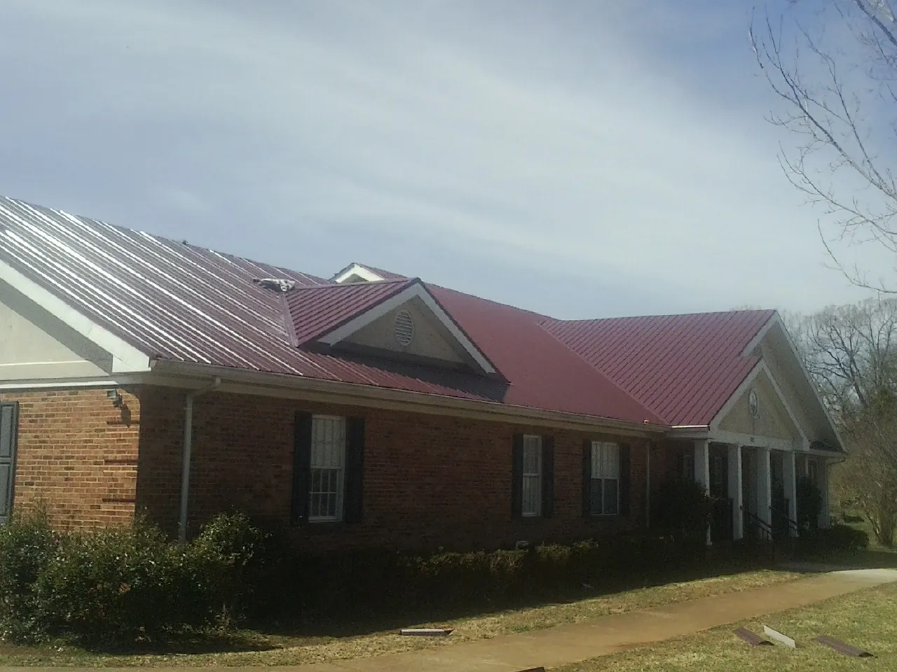 Red metal roof with gabled entries on a long brick building, from a Hail Damage Roof Repair job in Mont Alto