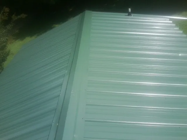 New green metal panels meeting at the ridge of a roof — Flat Roof Repair work by our crew in Mont Alto