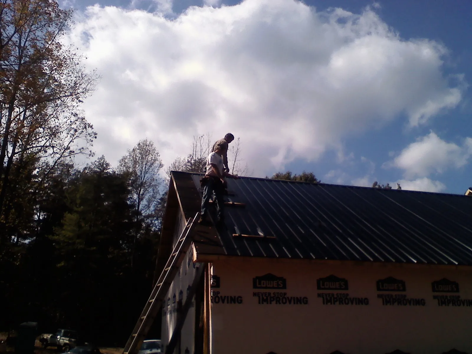 Roofer fastening dark metal panels high against a cloudy sky, from a Roof Inspection job in Mont Alto
