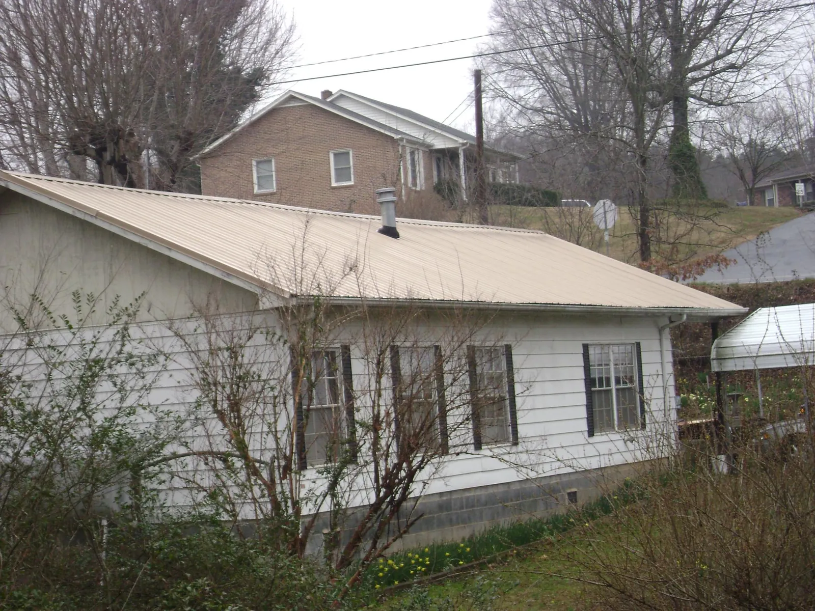 Tan metal roof on a white sided house set into a hillside — Commercial Roofing by Roofing Brothers in Mont Alto